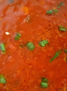 A thick red tomato sauce with green basil leaves olive oil and garlic