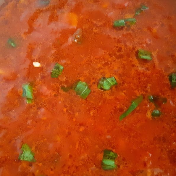 A thick red tomato sauce with green basil leaves olive oil and garlic