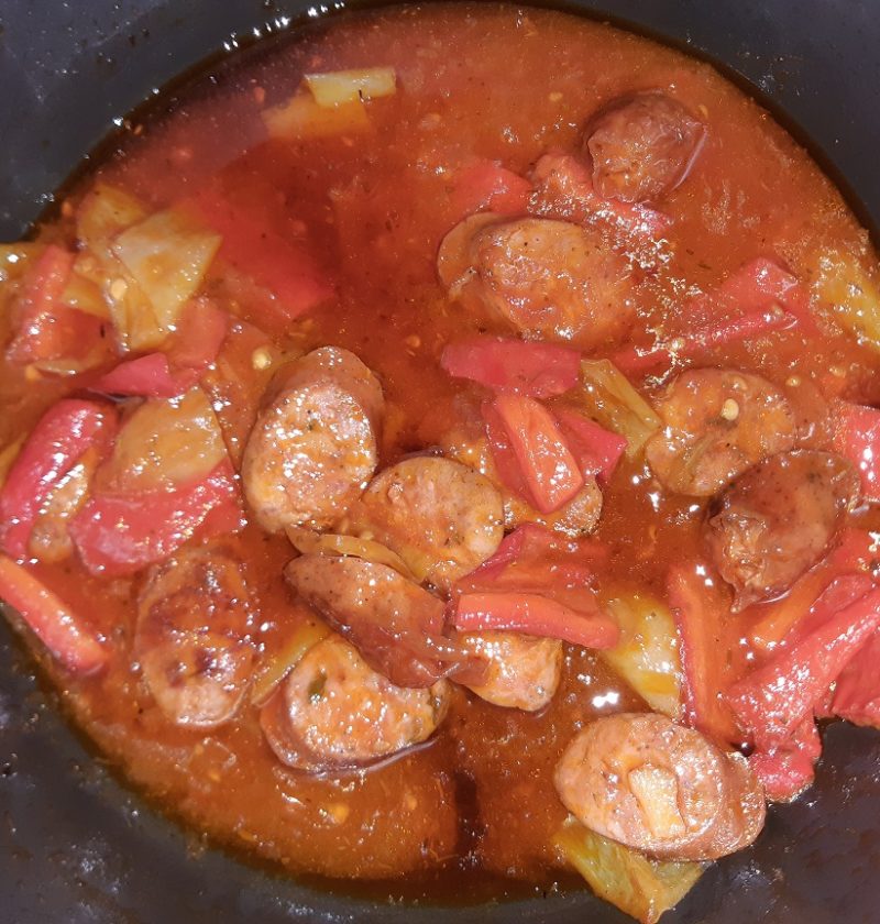 A meal with sliced sausages green and red peppers and tomato