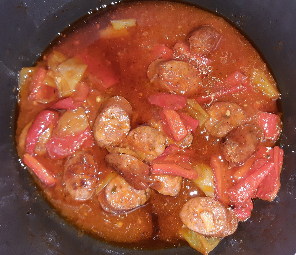 A meal with sliced sausages green and red peppers and tomato