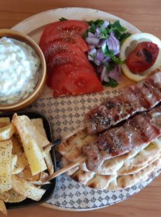 a wooden plateau with meat on skewers french fries tomatoes onion and parsley salad and pitta bread