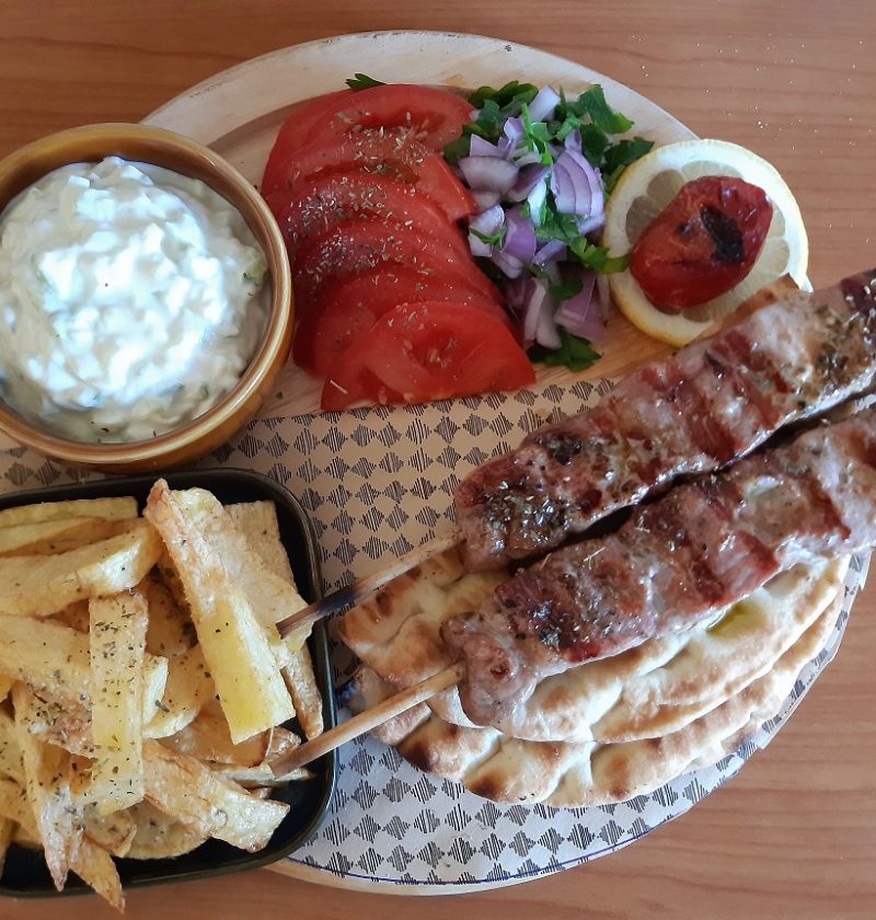 a wooden plateau with meat on skewers french fries tomatoes onion and parsley salad and pitta bread
