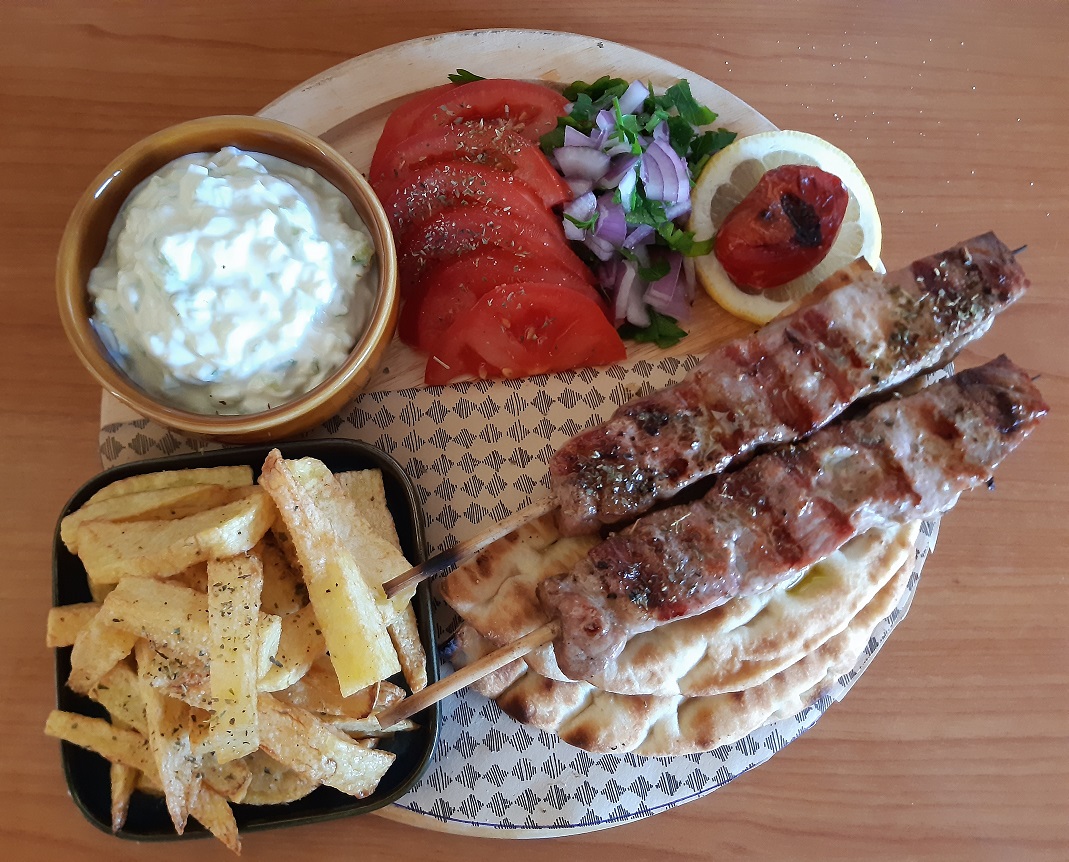 a wooden plateau with meat on skewers french fries tomatoes onion and parsley salad and pitta bread