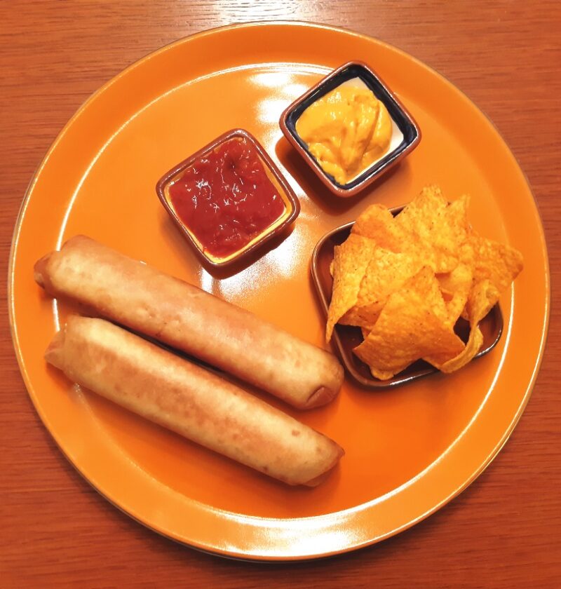 A dish with two crisp chicken burittos served with nachos salsa and cheese sauce