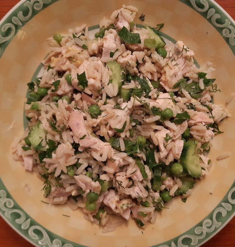 A salad dish with a mix of rice, chicken, peas