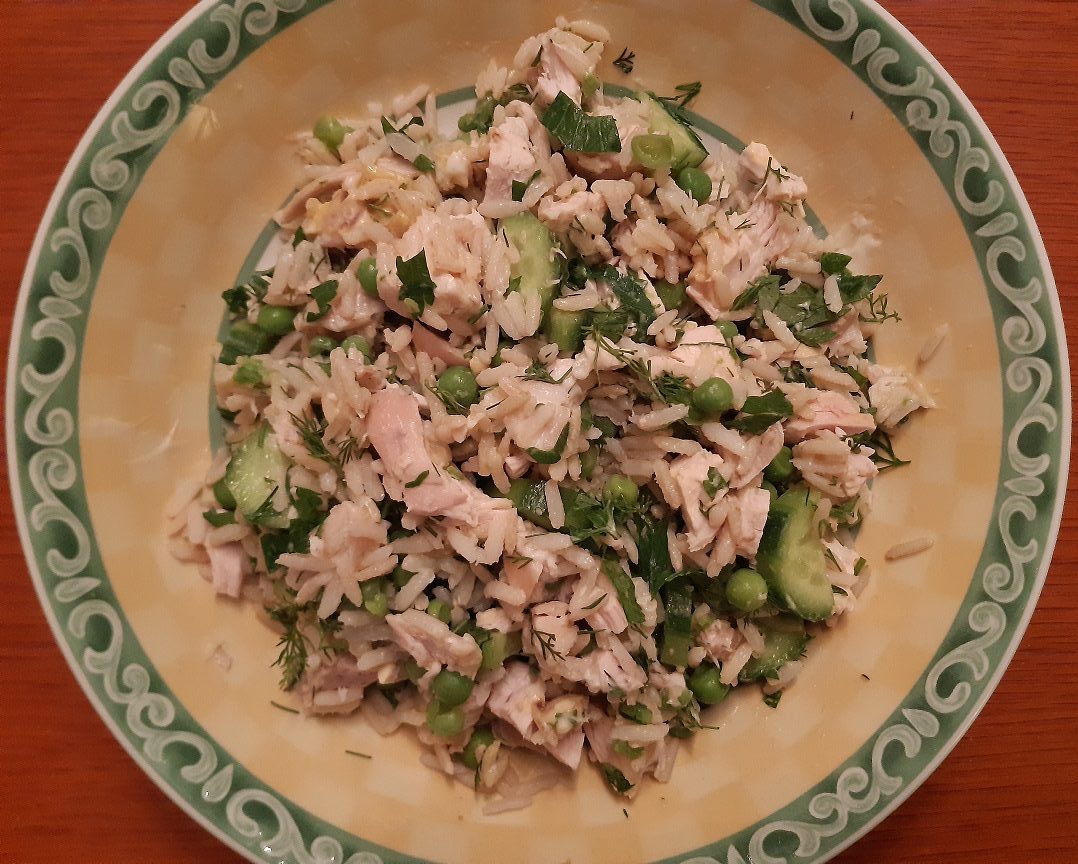 A salad dish with a mix of rice, chicken, peas