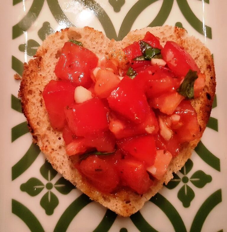 A heart shaped slice of bread with tomatoes garlic and basil