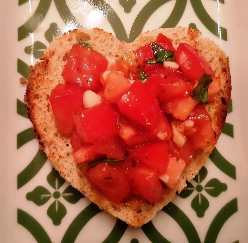 A heart shaped slice of bread with tomatoes garlic and basil