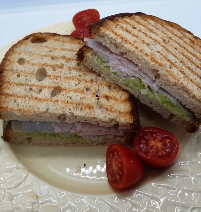 A dish with a turkey avocado sandwich and cherry tomatoes