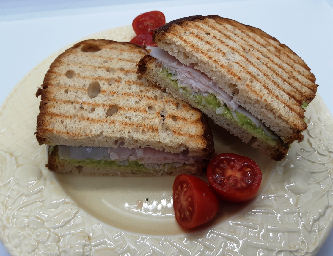 A dish with a turkey avocado sandwich and cherry tomatoes