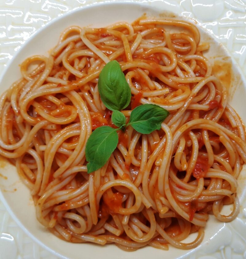 A dish with spaghetti with red tomato sauce and basil