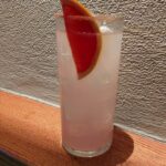 a long drink glass with a pink alcohol drink and grapefruit.