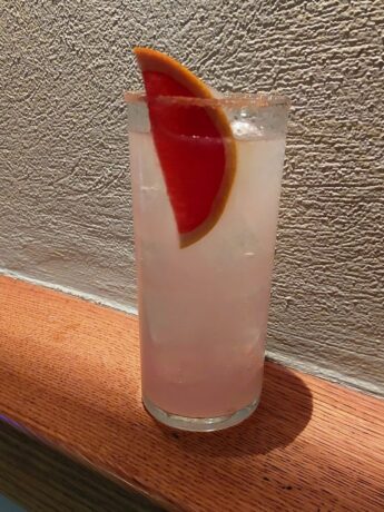 a long drink glass with a pink alcohol drink and grapefruit.