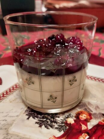 A festive glass with white panna cotta dessert tpped with berries