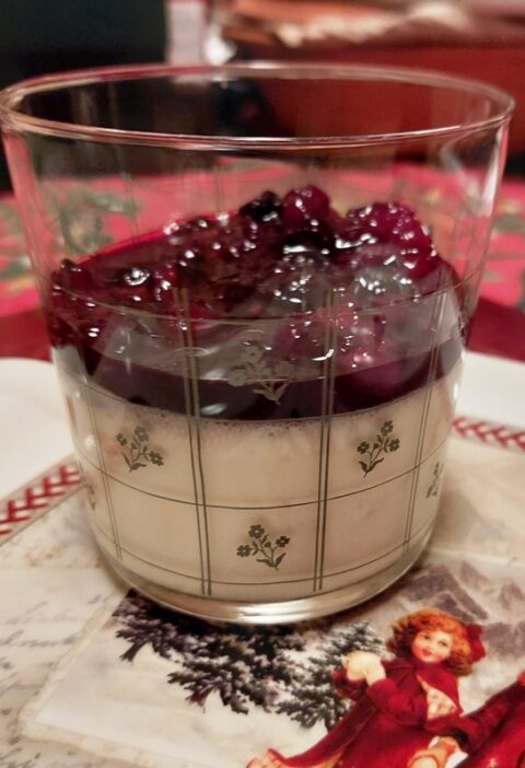 A festive glass with white panna cotta dessert tpped with berries