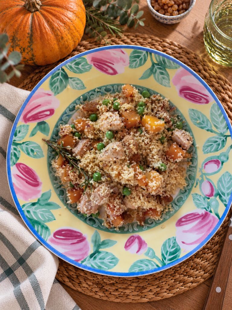Warm pumpkin salad with couscous, chicken, green peas, raisins and rosemary, served on a colourful floral plate.
